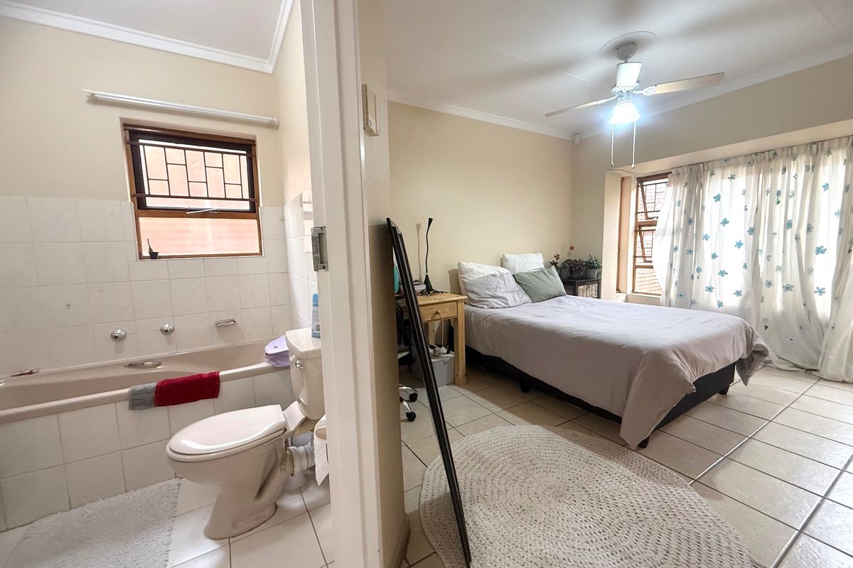 A bedroom featuring tiled flooring and a ceiling fan, with an adjoining bathroom equipped with a built-in bathtub and toilet.