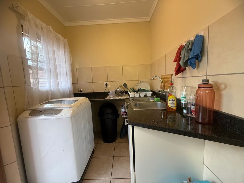 Functional laundry area featuring granite countertops, a double basin sink, and tiled splashbacks, providing a practical space for household chores.
