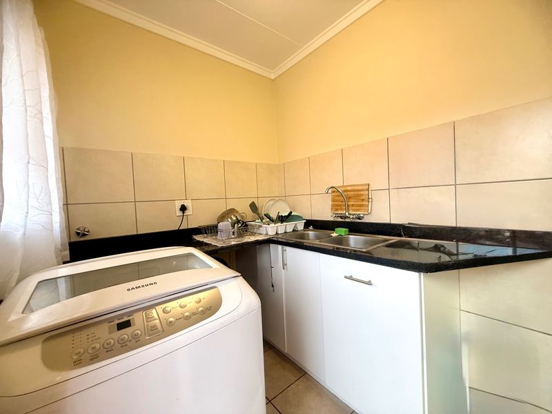 Functional laundry area featuring built-in white cabinetry, granite countertops, a double stainless steel sink, and tiled backsplash.