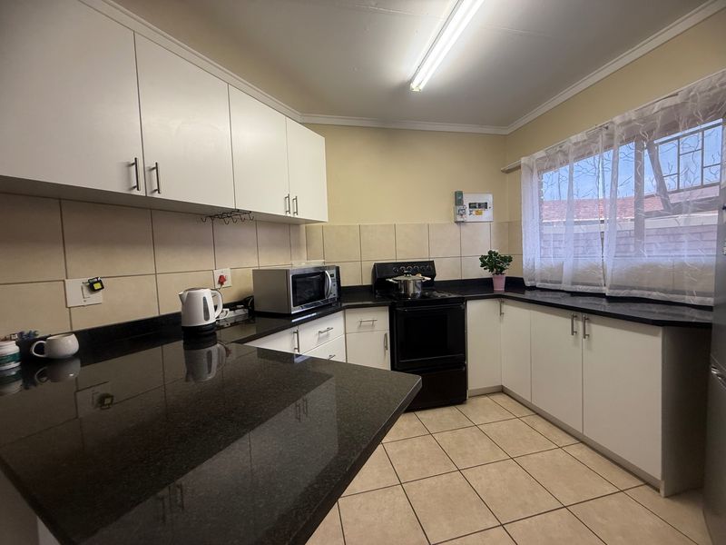 A functional kitchen featuring white cabinetry, dark granite countertops, tiled backsplash, and ceramic floor tiles with a window providing natural light.