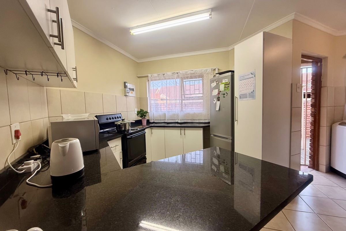 Functional kitchen featuring dark granite countertops, ample built-in cabinetry, tiled backsplash, and an electric stove, with direct access to an adjacent utility area.
