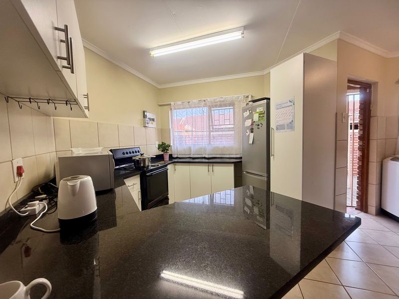 Functional kitchen featuring dark granite countertops, ample built-in cabinetry, tiled backsplash, and an electric stove, with direct access to an adjacent utility area.