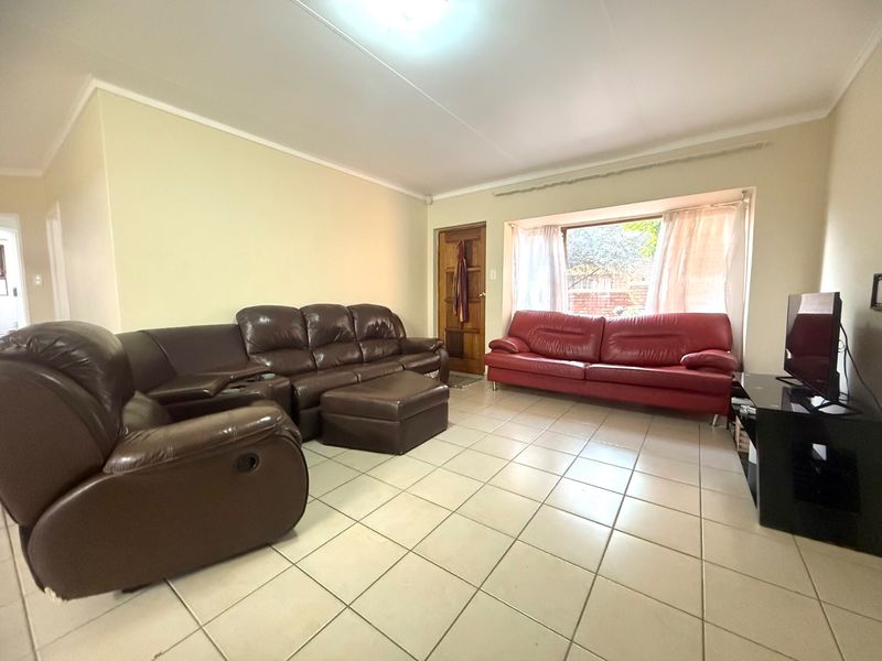 Spacious living room featuring neutral tiled flooring, a large bay window providing natural light, and a classic timber entrance door.
