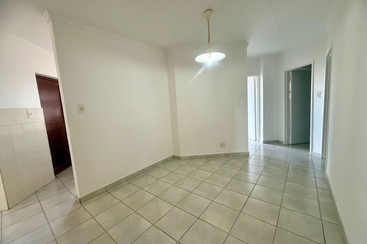 An empty, neutrally finished living area featuring ceramic floor tiles, a central pendant light, and access to adjacent rooms.