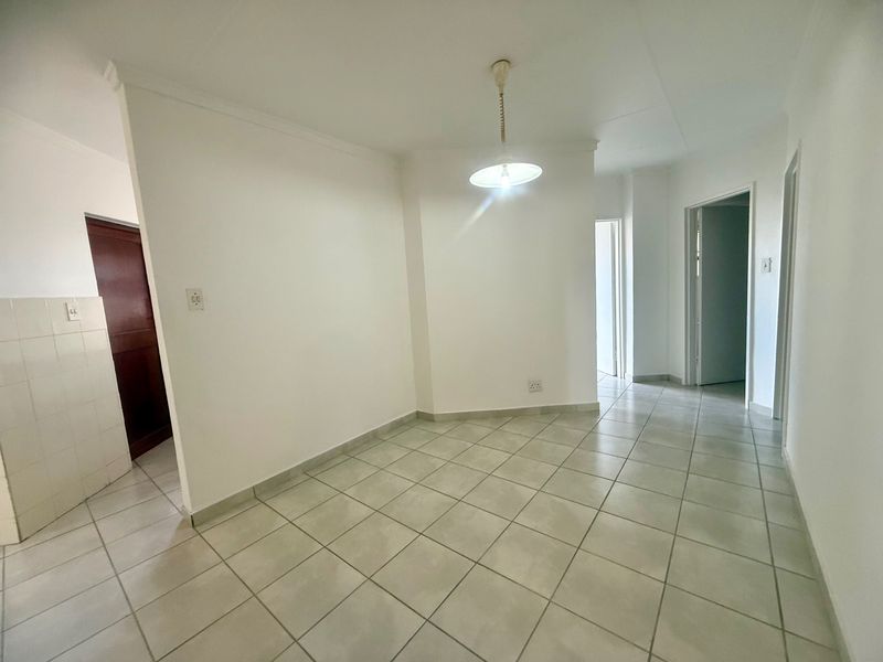 An empty, neutrally finished living area featuring ceramic floor tiles, a central pendant light, and access to adjacent rooms.