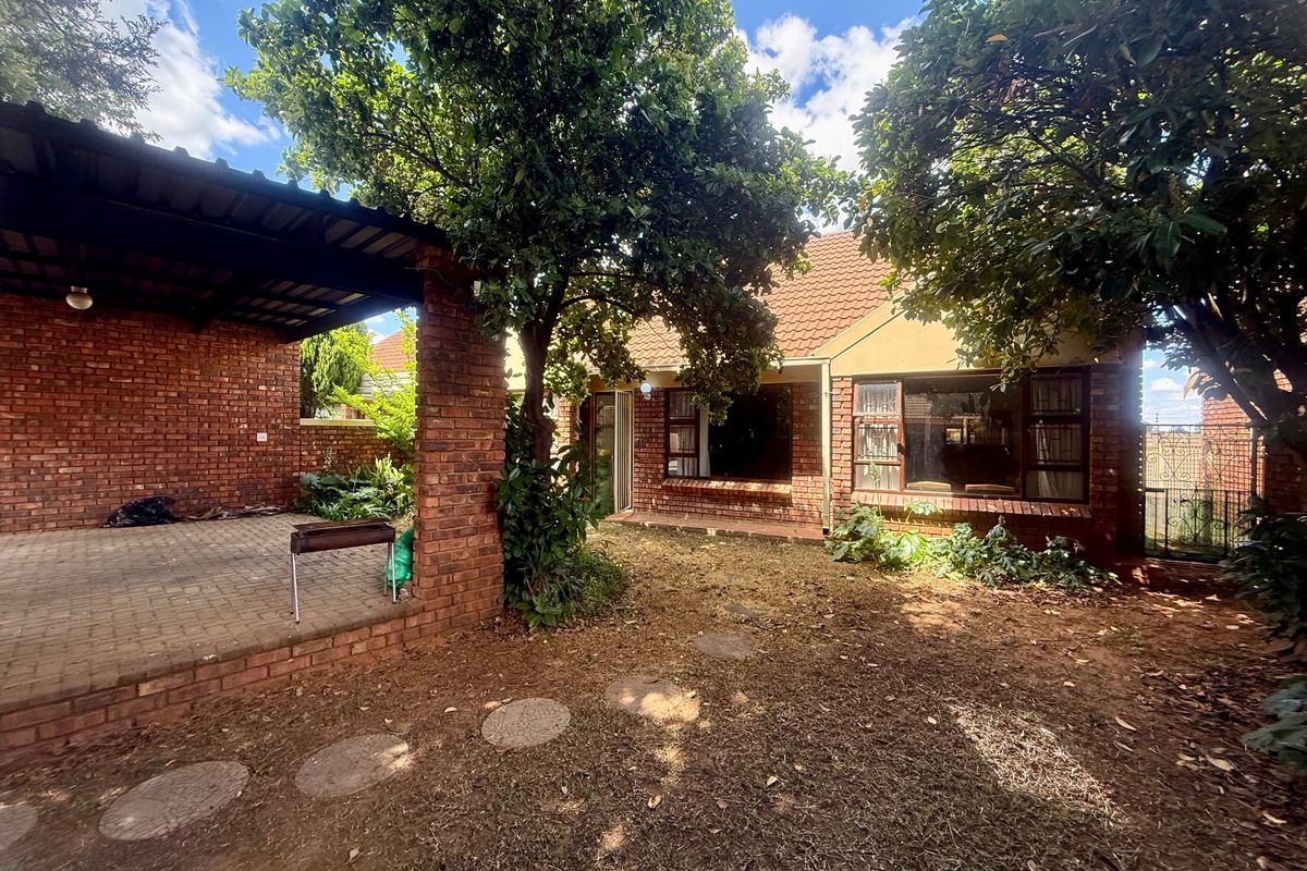 Rear view of the townhouse featuring a covered brick patio, established trees, and a private garden area with paved stepping stones.