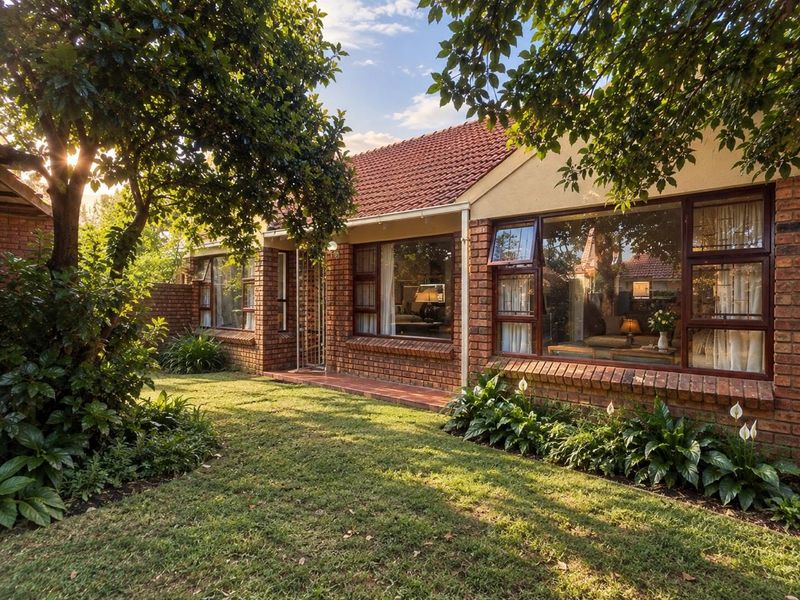 A well-maintained townhouse rear elevation featuring classic face brick construction, large windows, and a lush, established garden setting.