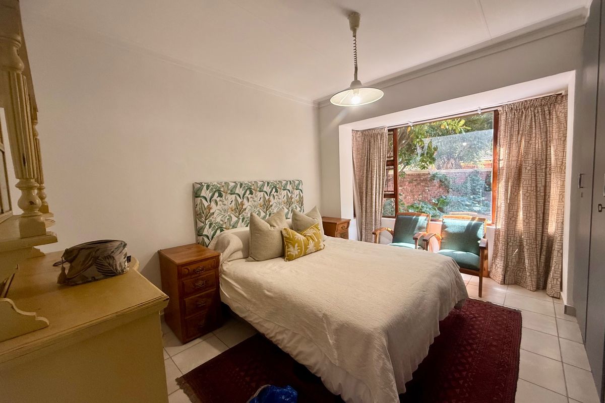 A well-lit bedroom featuring tiled flooring, a built-in wardrobe, and a large window overlooking the garden area.