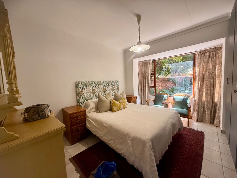 A well-lit bedroom featuring tiled flooring, a built-in wardrobe, and a large window overlooking the garden area.