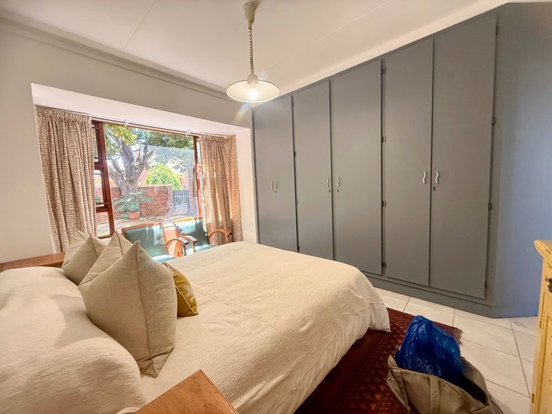 A spacious bedroom featuring extensive built-in cupboards, tiled flooring, and a large window providing natural light and garden views.
