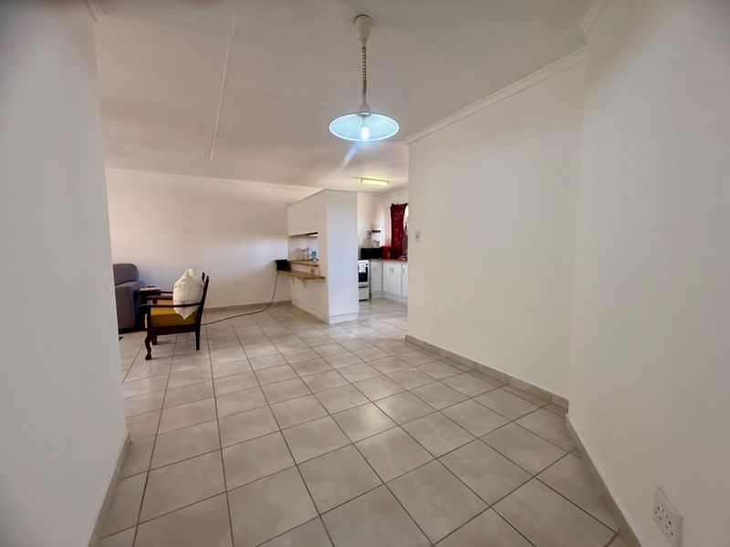 An open-plan living and kitchen area featuring neutral tiled flooring, a breakfast bar, and functional kitchen cabinetry.