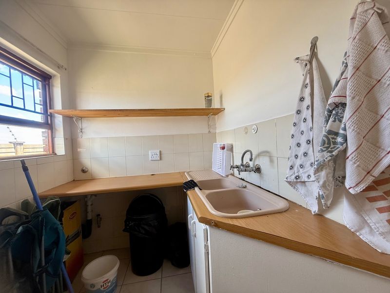 Functional laundry area featuring a double basin sink, laminate countertops, tiled splashback, and wall-mounted shelving for storage.
