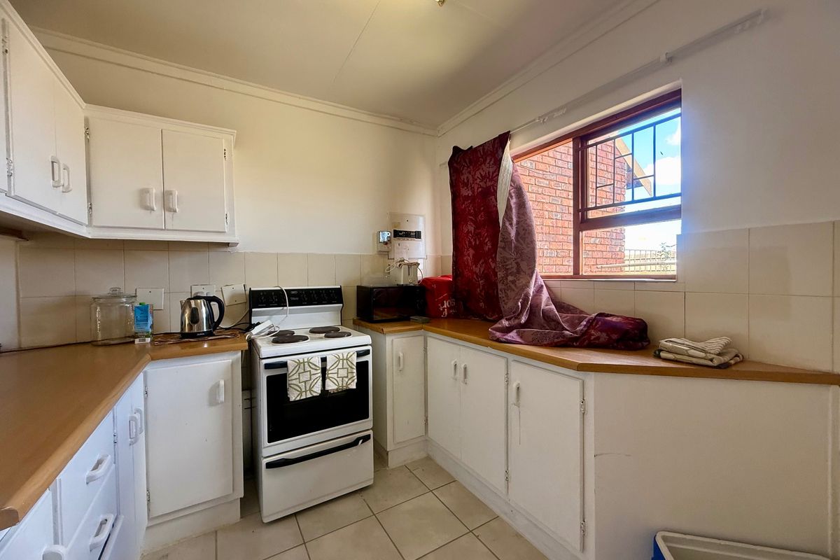 A functional kitchen featuring white cabinetry, laminate countertops, tiled backsplash, and a freestanding stove, offering potential for modernization.