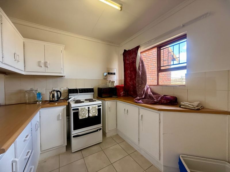 A functional kitchen featuring white cabinetry, laminate countertops, tiled backsplash, and a freestanding stove, offering potential for modernization.