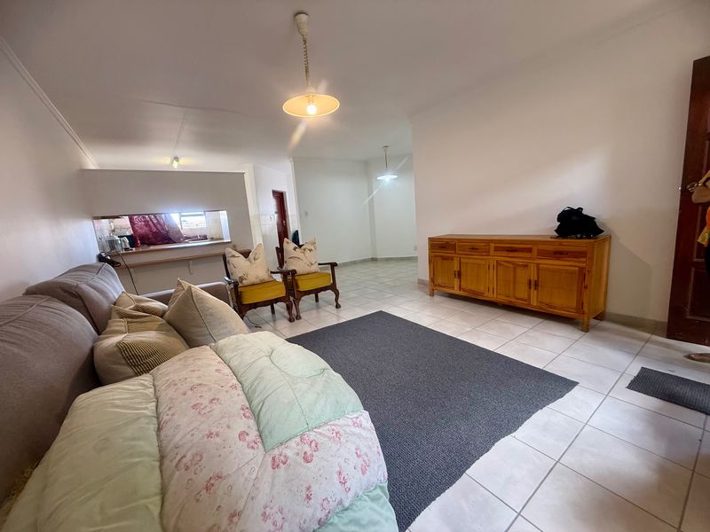 Open plan living area featuring tiled flooring, a pass-through window to the kitchen, and neutral wall finishes.