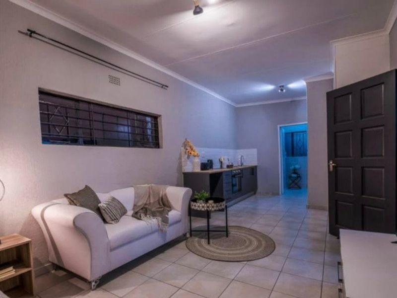 Open-plan living area featuring tiled flooring, neutral walls, and a compact kitchen with built-in cabinetry and oven.