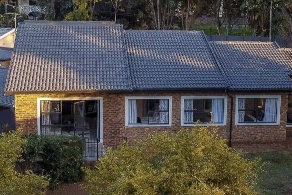 Rear view of a facebrick house featuring a tiled roof, aluminium window frames, and sliding glass doors opening onto a garden area.