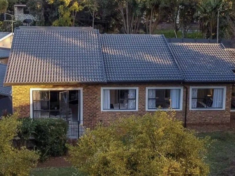 Rear view of a facebrick house featuring a tiled roof, aluminium window frames, and sliding glass doors opening onto a garden area.