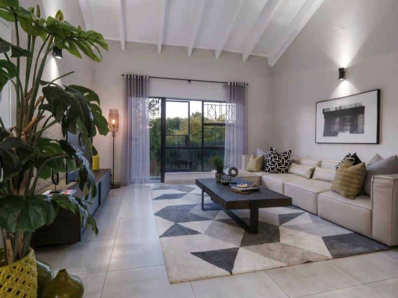 Spacious living room featuring a high vaulted ceiling with exposed rafters, tiled flooring, and a large sliding glass door providing natural light.