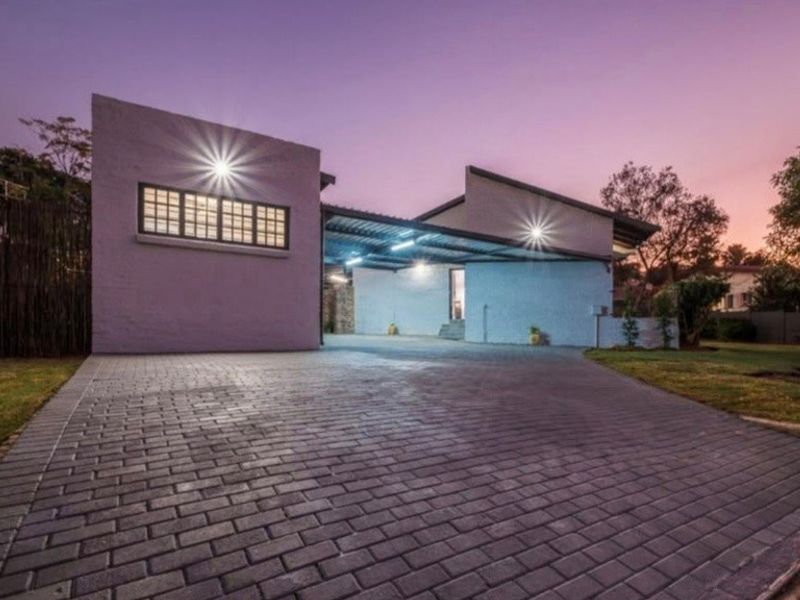 A modern front exterior view featuring a spacious paved driveway, a covered carport area, and contemporary architectural roof lines at dusk.