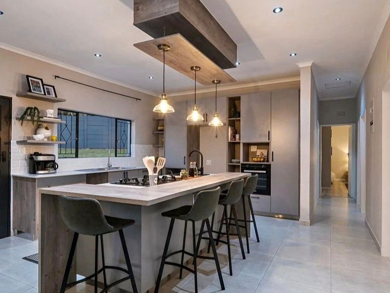 Modern kitchen featuring a central island with integrated hob, sleek cabinetry, built-in oven, and contemporary lighting fixtures, finished with high-quality tiled flooring.