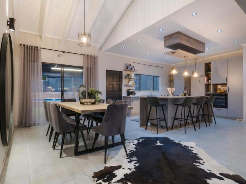 Spacious open-plan living and dining area featuring a modern kitchen with a large island, vaulted ceilings with exposed beams, and direct access to the patio.