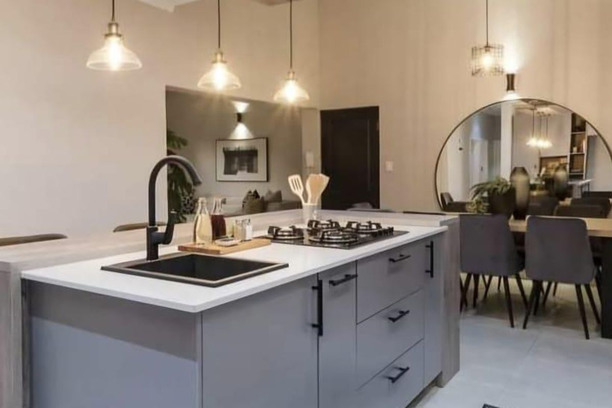 Modern kitchen featuring a central island with a gas hob, undermount sink, and contemporary pendant lighting, seamlessly integrated into an open-plan living space.
