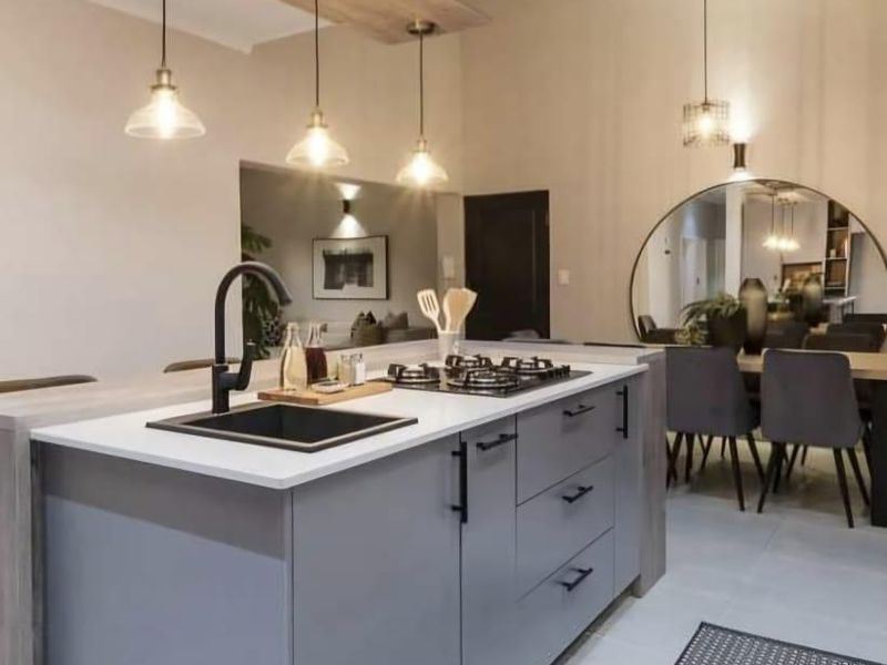 Modern kitchen featuring a central island with a gas hob, undermount sink, and contemporary pendant lighting, seamlessly integrated into an open-plan living space.