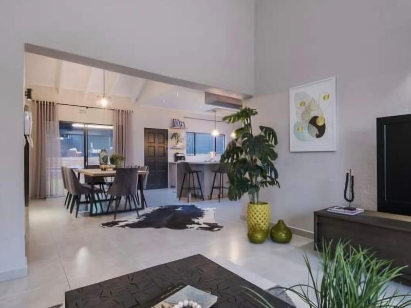 Spacious open-plan living and dining area featuring high vaulted ceilings, neutral tiled flooring, and a modern kitchen island with seamless flow to the patio.