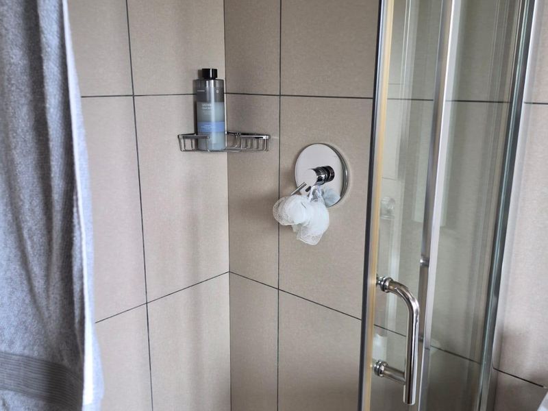 A clean and functional shower enclosure featuring neutral wall tiles, a glass door, and a modern chrome shower mixer.
