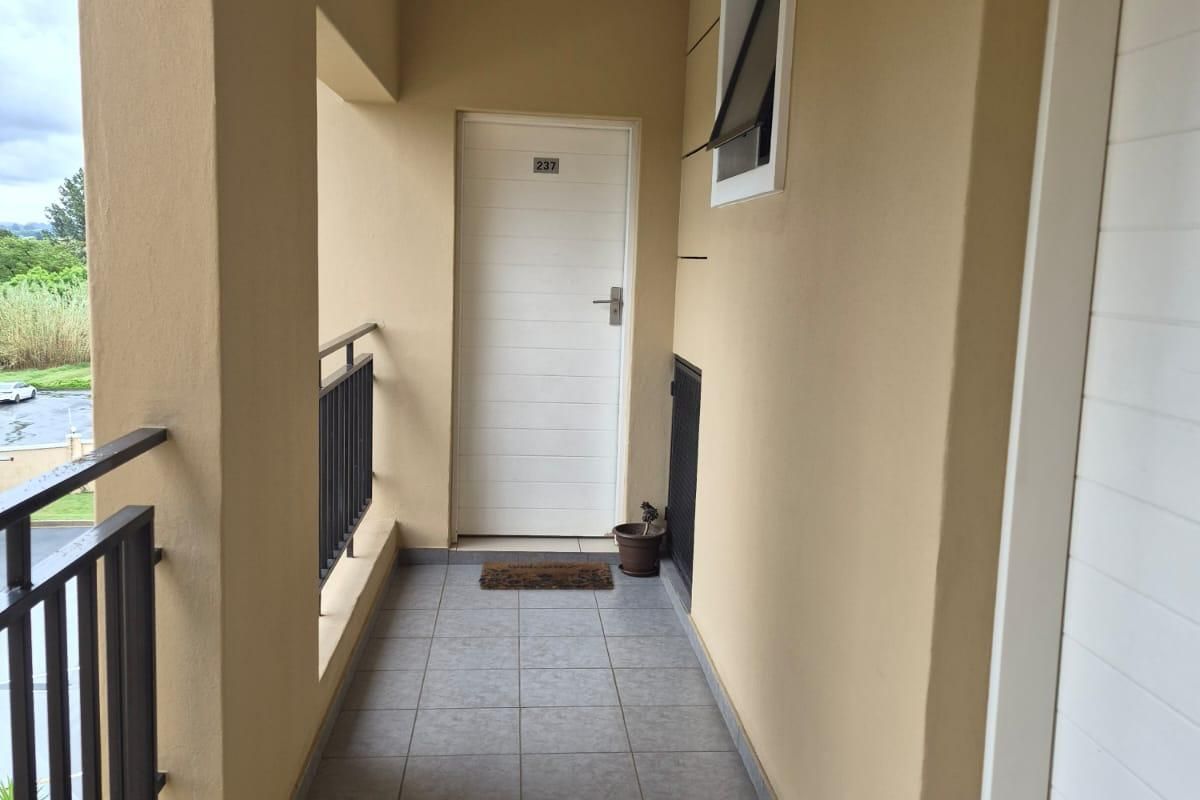 A clean, covered apartment balcony featuring tiled flooring and a metal balustrade, providing a private entrance area.
