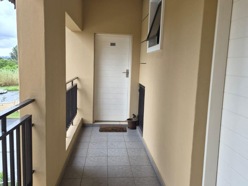 A clean, covered apartment balcony featuring tiled flooring and a metal balustrade, providing a private entrance area.