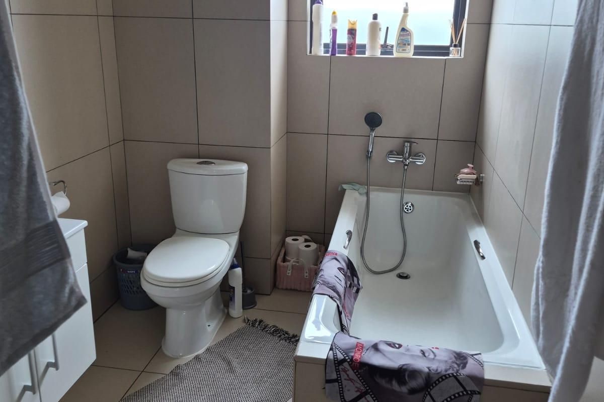 A functional bathroom featuring full-height wall tiling, a built-in bathtub with a handheld shower mixer, a toilet, and a vanity cabinet.
