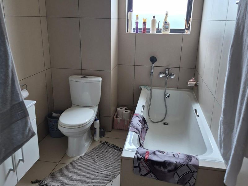 A functional bathroom featuring full-height wall tiling, a built-in bathtub with a handheld shower mixer, a toilet, and a vanity cabinet.