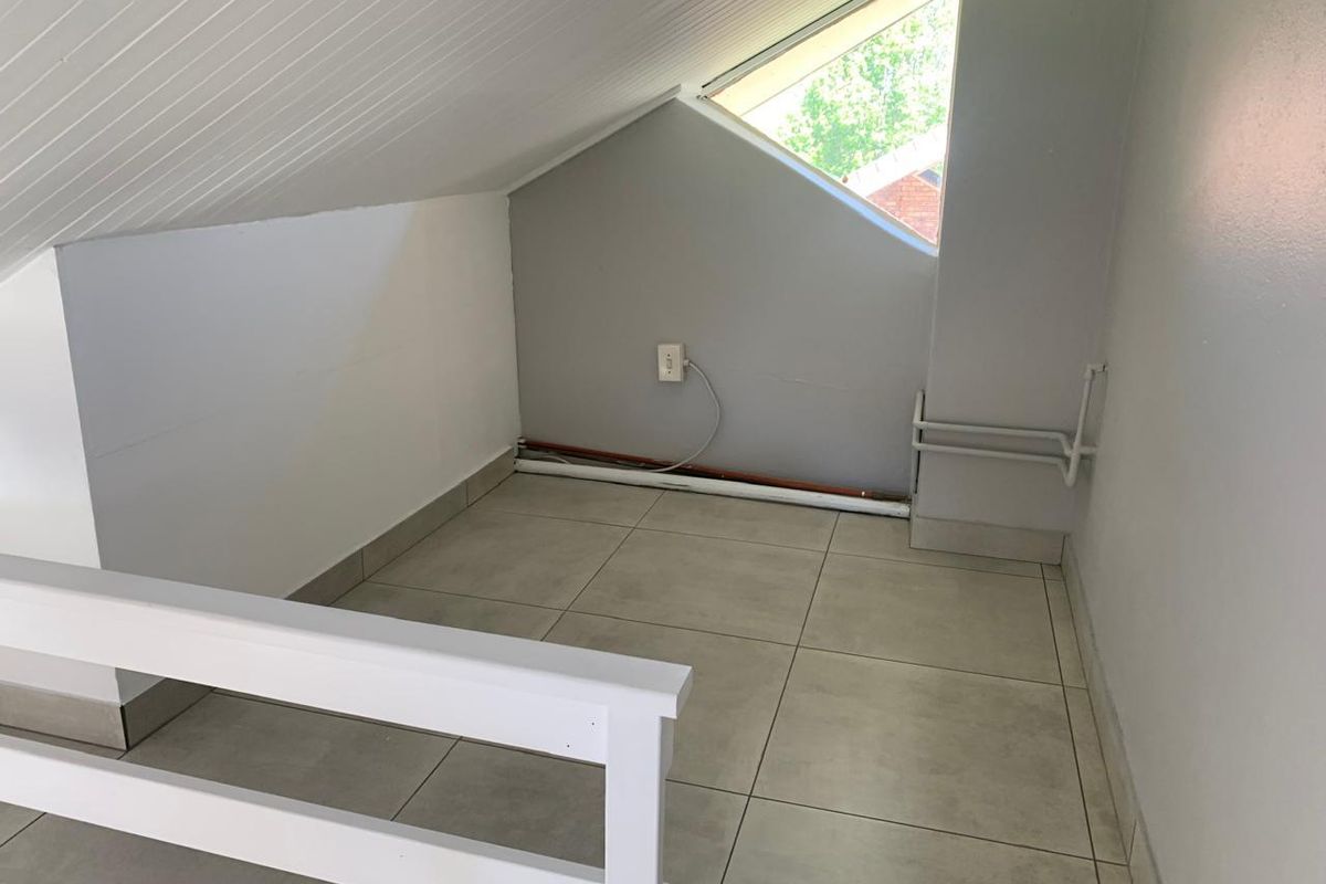 An empty attic-style bedroom featuring tiled flooring, a sloped ceiling, and a unique triangular window, offering a compact and versatile living space.