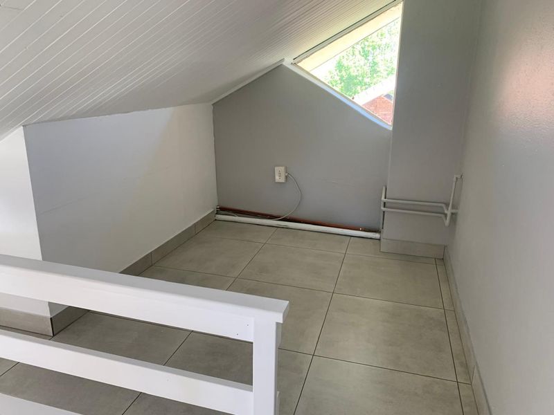 An empty attic-style bedroom featuring tiled flooring, a sloped ceiling, and a unique triangular window, offering a compact and versatile living space.