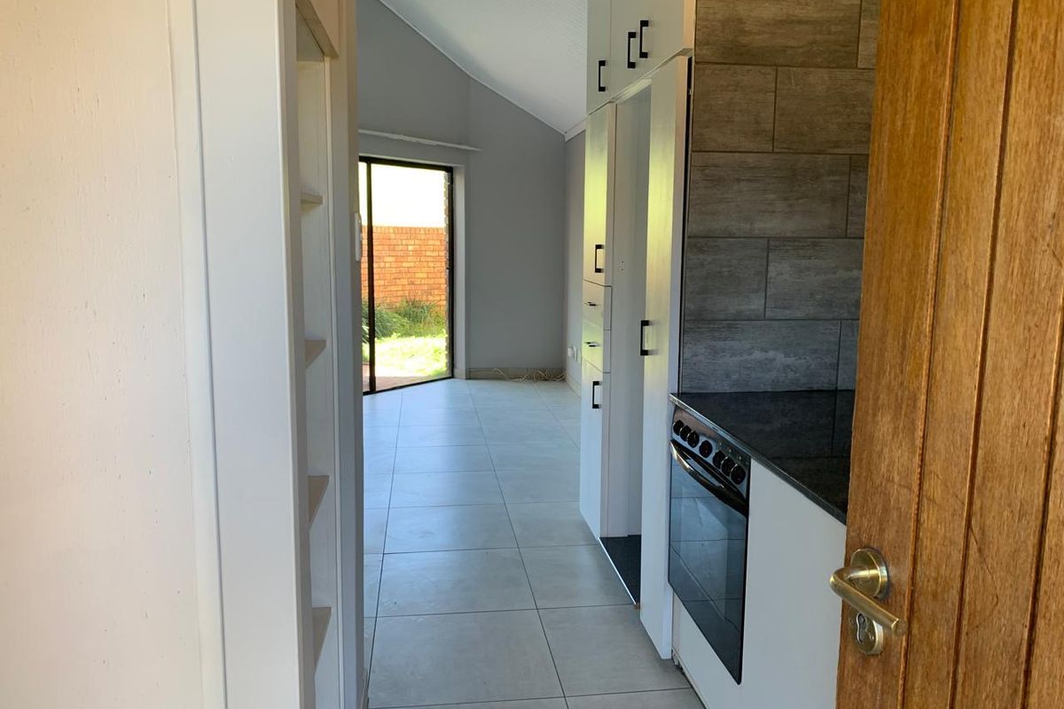 A modern, open-plan kitchen featuring sleek white cabinetry, dark stone countertops, and tiled finishes, leading directly to an outdoor patio area.