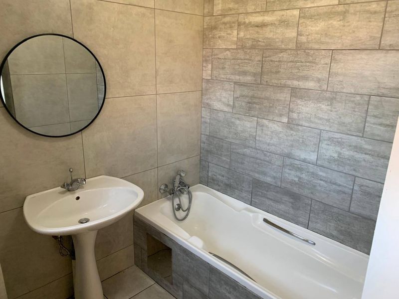 Modern bathroom featuring a pedestal basin, bathtub with handheld shower attachment, and contemporary neutral-toned wall and floor tiling.