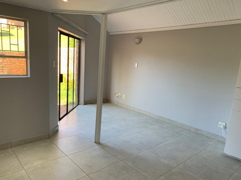 A bright, empty living area featuring neutral tiled flooring, a tongue and groove ceiling, and direct access to the garden through a sliding glass door.