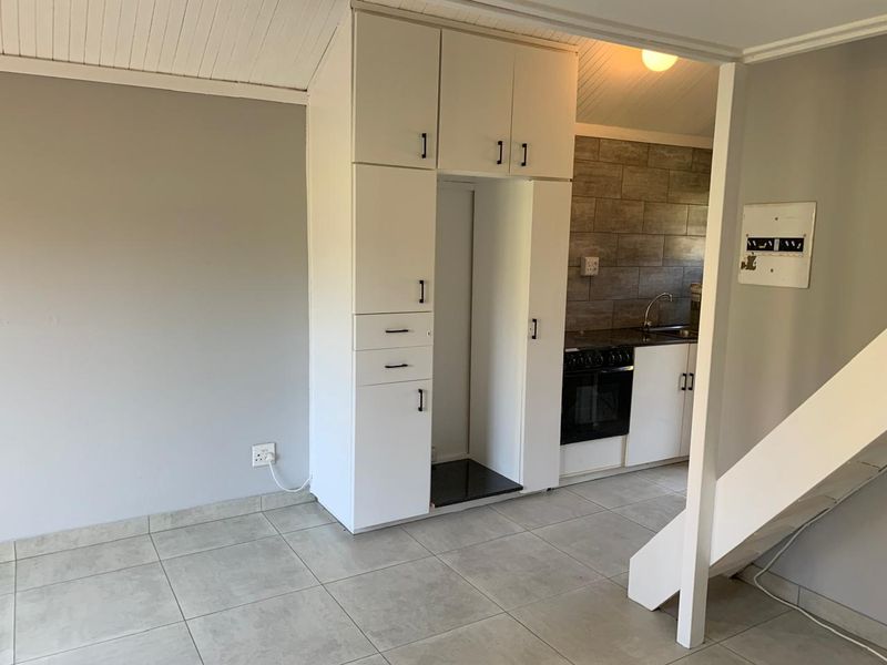 An open-plan living and kitchen area featuring tiled flooring, built-in cabinetry, and a functional kitchen setup with a built-in oven and hob.