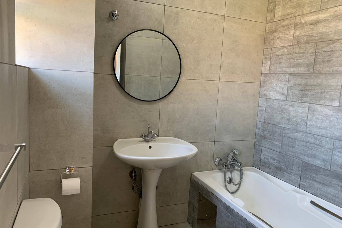 Modern bathroom featuring a pedestal basin, bathtub with handheld shower attachment, and contemporary neutral-toned ceramic wall tiling.