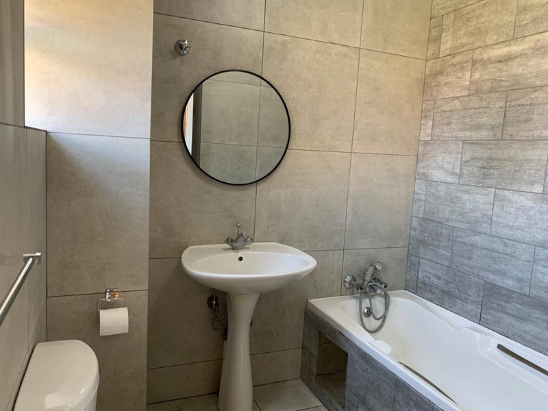 Modern bathroom featuring a pedestal basin, bathtub with handheld shower attachment, and contemporary neutral-toned ceramic wall tiling.