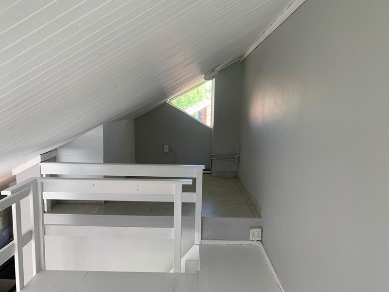 An attic-style bedroom featuring a sloped timber-paneled ceiling, tiled flooring, and a unique triangular window, providing a cozy and versatile living space.