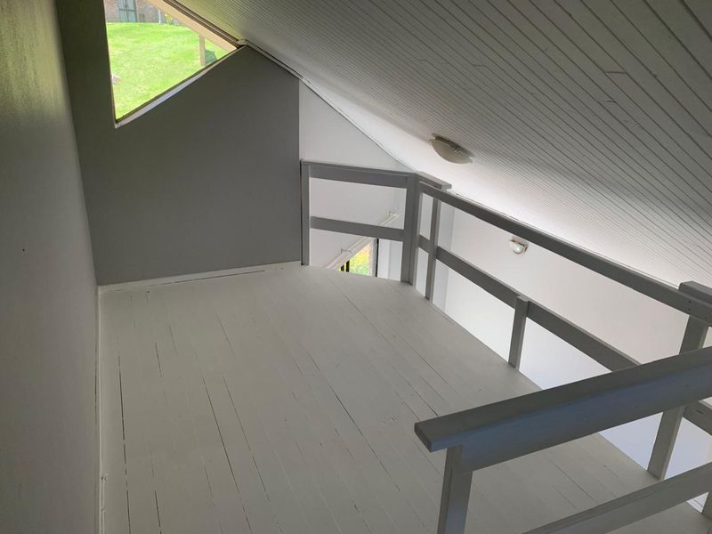 An open loft-style mezzanine area featuring a sloped timber ceiling, painted wooden flooring, and a protective timber balustrade overlooking the lower level.