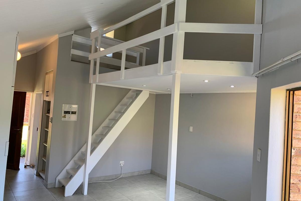Open plan living area featuring a mezzanine loft level with a wooden staircase, recessed lighting, and neutral tiled flooring.