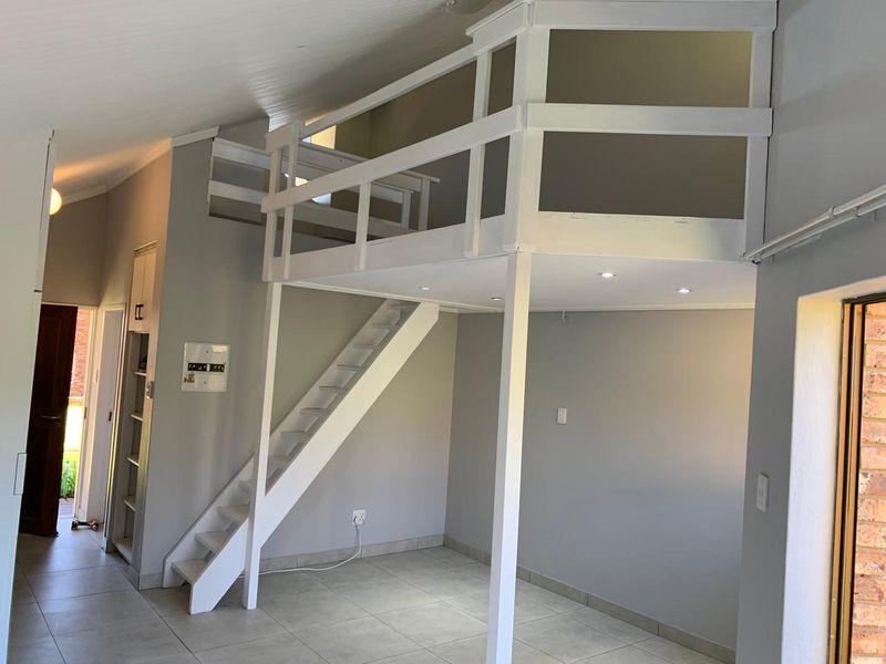 Open plan living area featuring a mezzanine loft level with a wooden staircase, recessed lighting, and neutral tiled flooring.