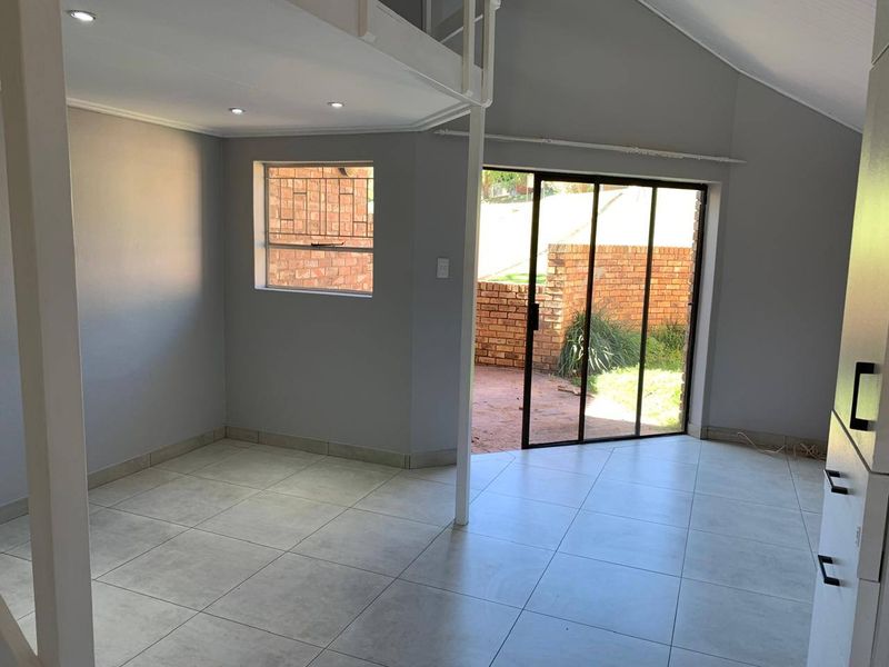 Bright open-plan living area featuring neutral tiled flooring, recessed lighting, and a mezzanine level, with direct access to an outdoor patio area.