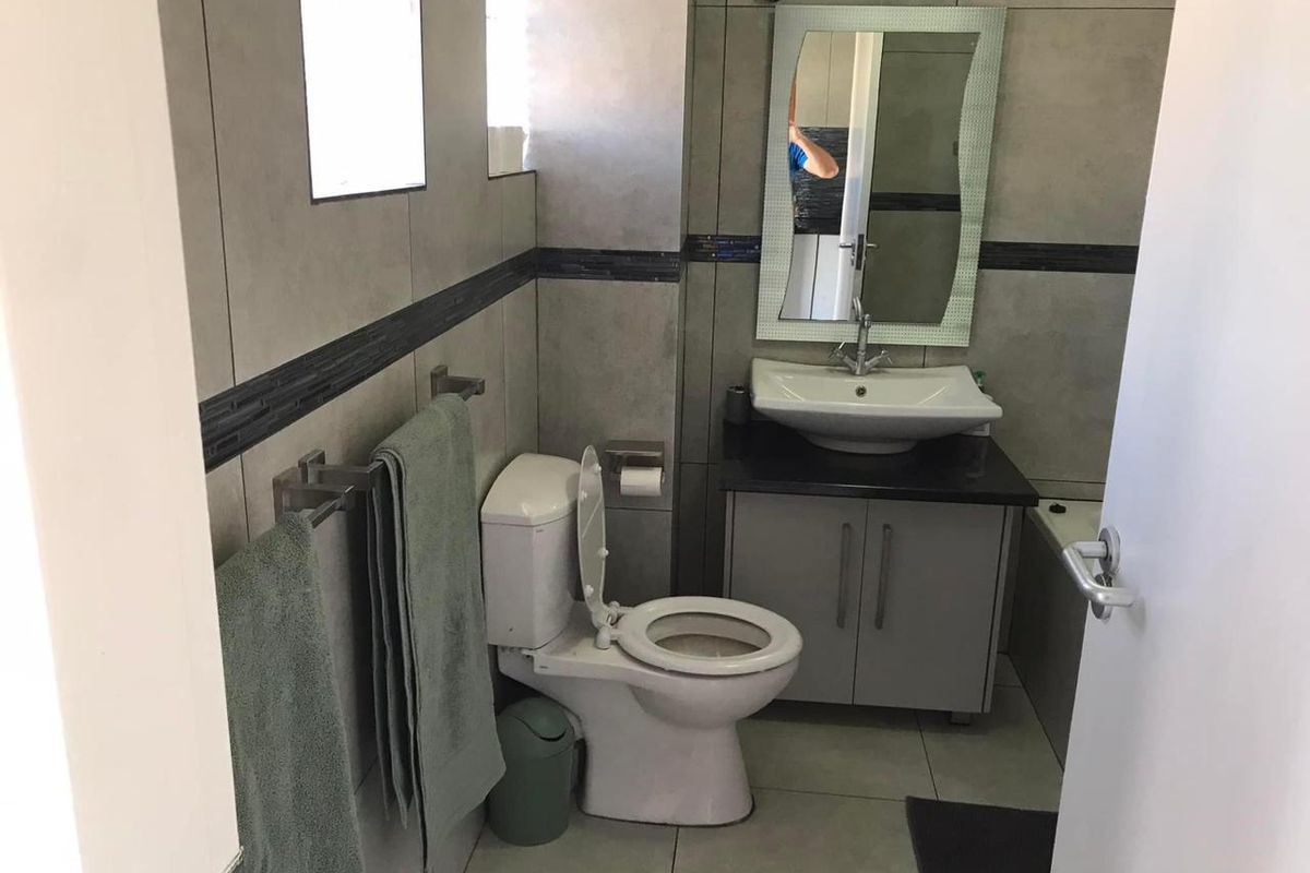 A functional bathroom featuring a modern vanity with basin, wall-mounted mirror, toilet, and neutral grey wall and floor tiling.
