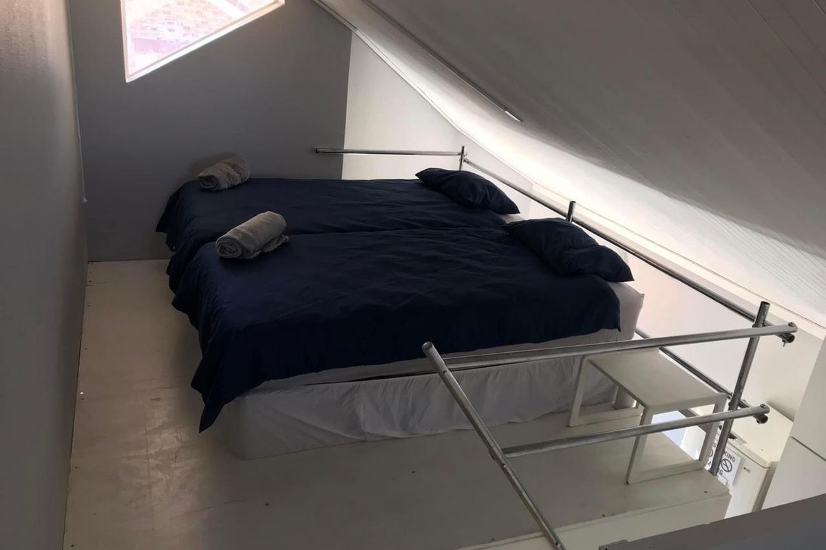 A loft-style bedroom featuring a sloped ceiling, a triangular window, and a metal safety railing overlooking the lower level.