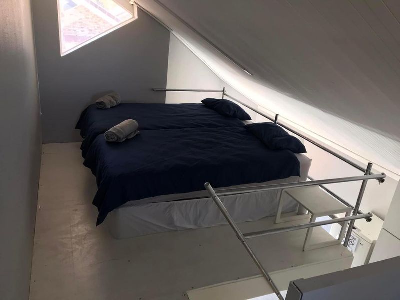 A loft-style bedroom featuring a sloped ceiling, a triangular window, and a metal safety railing overlooking the lower level.